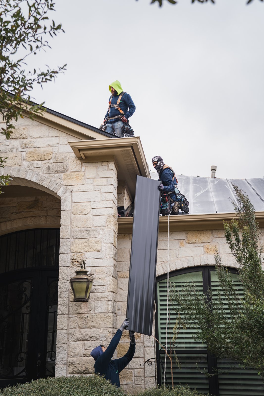 Hermes Roofing crew passing a standing seam metal panel up to the roof