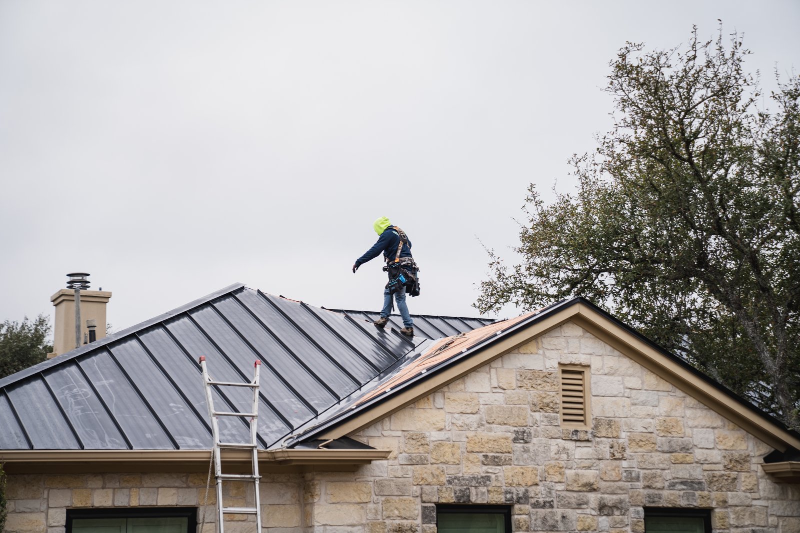 Roofer descending a new black standing seam metal roof on a stone home