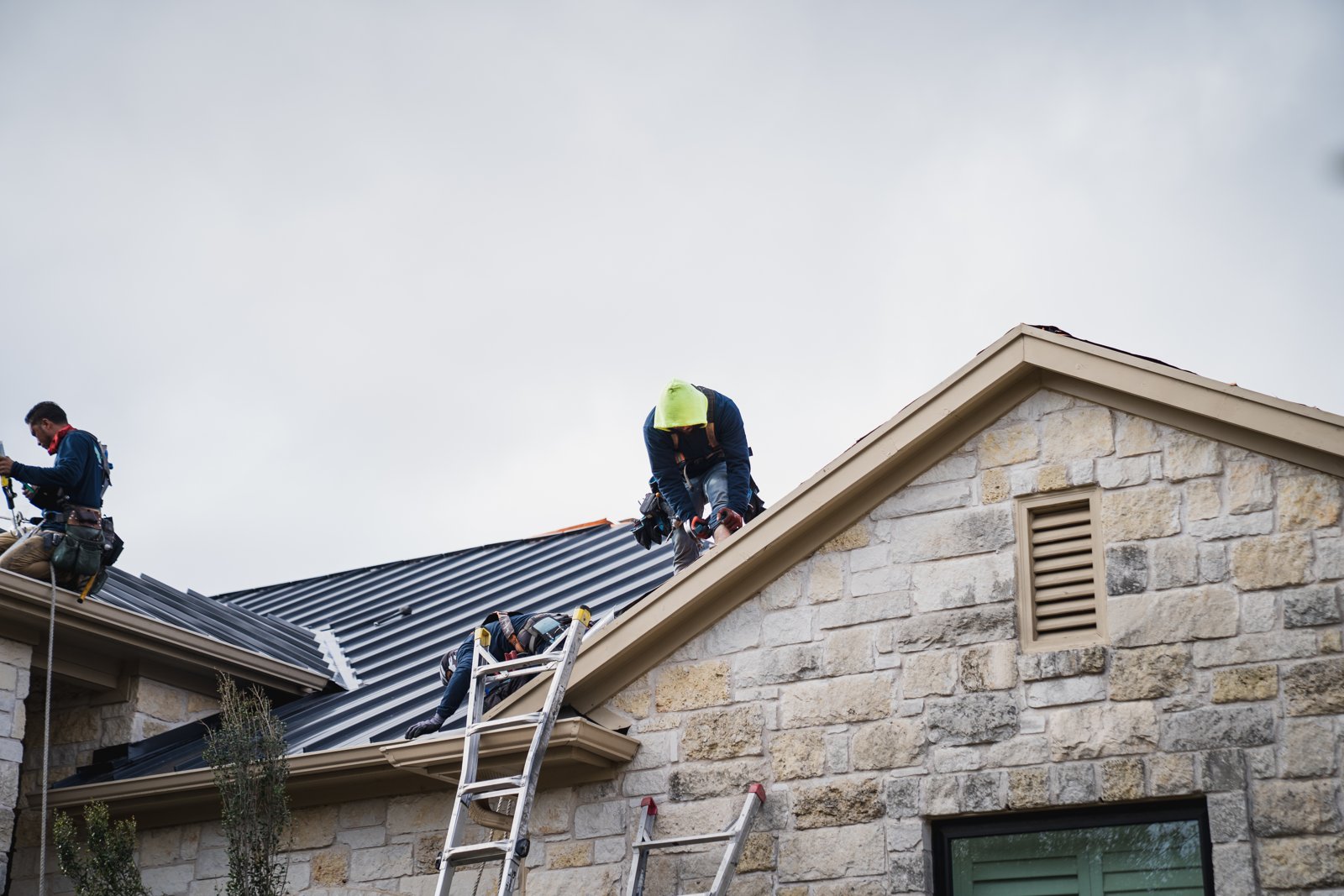 Hermes Roofing crew installing standing seam metal panels on a stone home in Driftwood, Texas